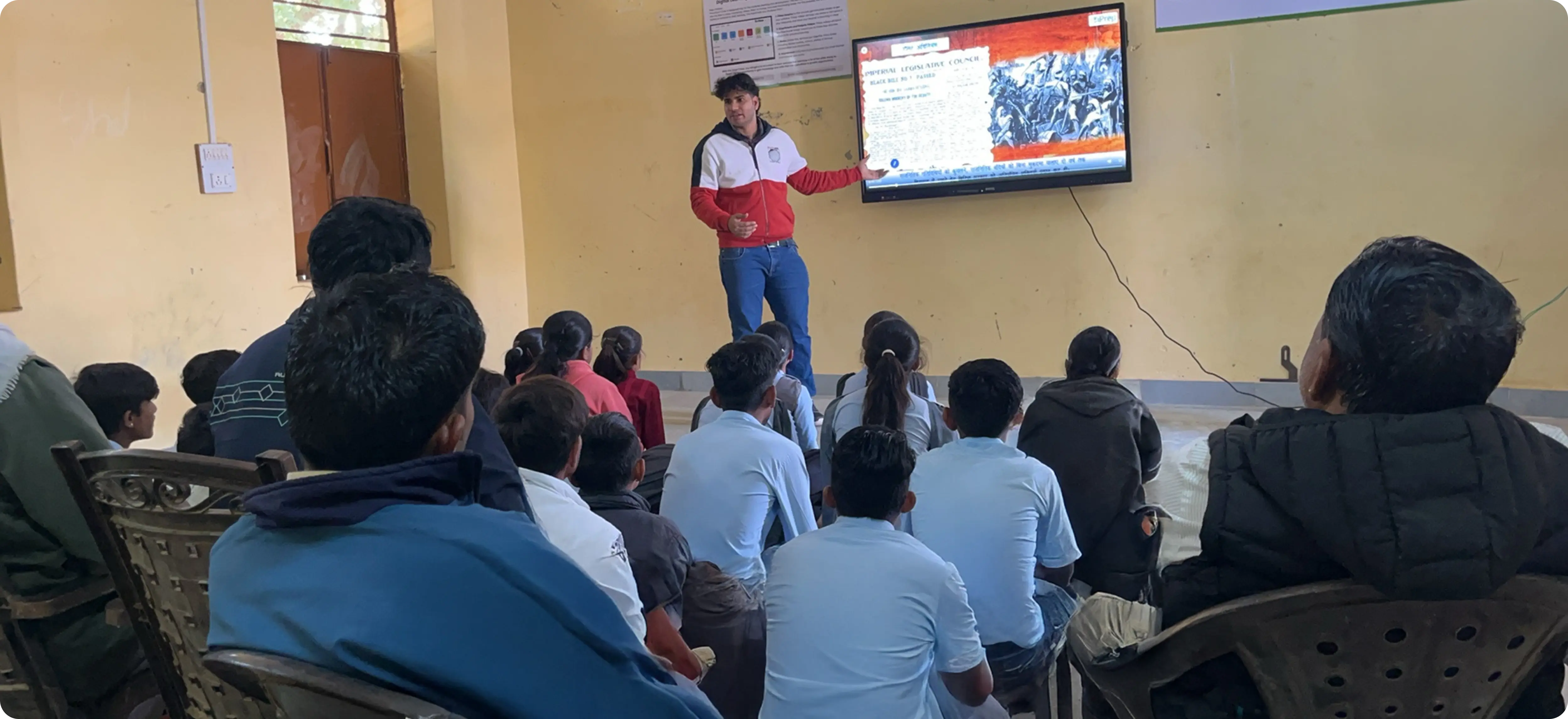 A teacher engaging with smart class content in Hindi on an interactive board in a classroom